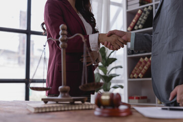 Obraz premium Two lawyers shaking hands in their office after reaching an agreement, with scales of justice and gavel on the table, symbolizing fairness, equality, and the legal process