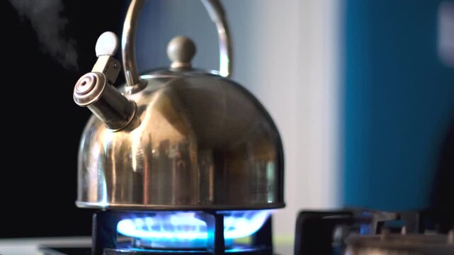 Blue gas flame of hob heats and boils water of whistling stainless steel kettle
