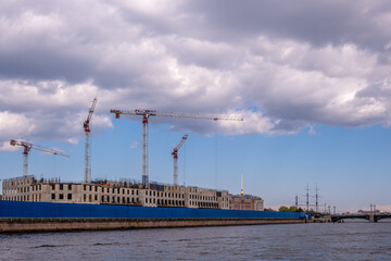 Naklejka premium Tower cranes at a construction site near the river against the sky.