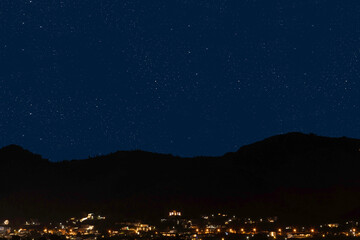 Bright Christmas star shining in the night sky above a peaceful town with mountains and illuminated houses.