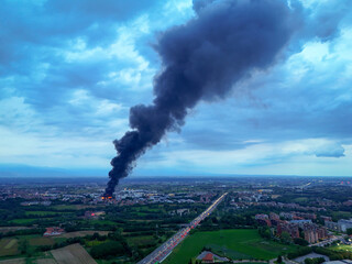 Pianezza, Italy - 04 September 2025: Aerial view of a thick plume of dark smoke billowing from the Euro Stamp plant, contrasting against the cloudy sky and distant cityscape.
