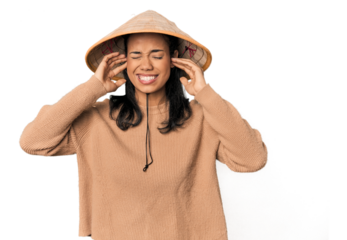 Young Filipina with Vietnamese hat covering ears with fingers, stressed and desperate by a loudly ambient.