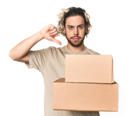Young man with cardboard boxes in studio showing a dislike gesture, thumbs down. Disagreement concept.