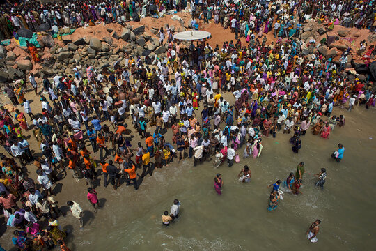 Puducherry, India - 28 February 2010: Aerial view of a vibrant crowd gathering along the rocky coastline, their colorful attire contrasting with the grey rocks and shimmering sea.
