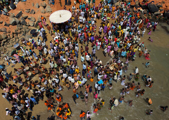 Puducherry, India - 28 February 2010: Aerial view of people gathered on the golden sands, a vibrant tapestry of colors contrasting with the azure sea and rocky shorelines.