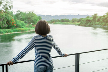 Woman standing on outdoor balcony overlooking peaceful river and mountain view, eco resort escape for digital detox, nature connection, and mental health wellness in sustainable travel.