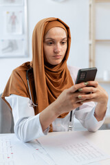 Young Muslim woman Doctor using Smartphone for chatting while sitting in clinic