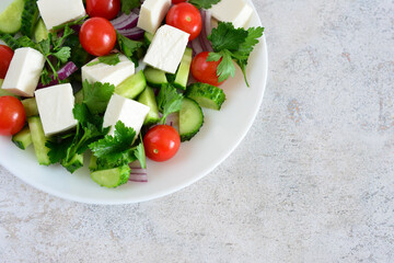 Fresh Greek salad with feta cheese, tomatoes and cucumbers on a white plate blank space