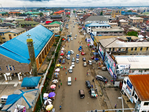 Port Harcourt, Nigeria - 15 November 2024: Aerial view of a bustling city street flanked by vibrant buildings and a prominent church, cars and people moving below a vast sky.