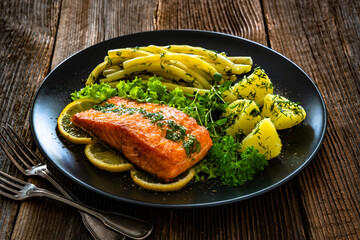 Fried salmon steak with yellow beans and boiled potatoes on wooden table	