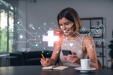 Smiling businesswoman in casual wear holding using smartphone typing at office workplace with notebook. Concept of distant work, business education. Medical healthcare icons hologram