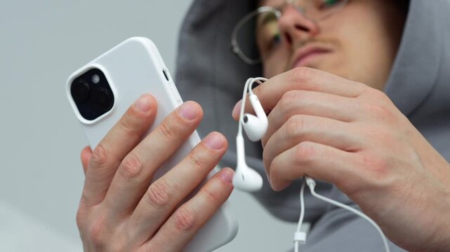 Man holding mobile wired headphones to listen to music.
Ear device for music and entertainment. Modern guy with mobile device and phone accessory in bright room