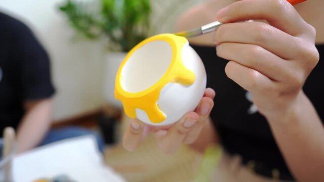 Creative hand painting a ceramic pot with bright yellow paint in a drip design, perfect for DIY art, home decoration, and craft inspiration in a modern artistic setting.