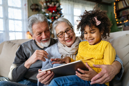 Happy grandparents enjoying time with African American grandchild, using tablet computer or e-book