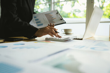 A businessman sits indoors at his office desk analyzing financial graphs on a laptop, planning...