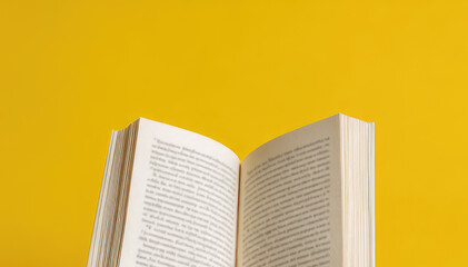 Fototapeta premium A hand holds an open book on a yellow background.