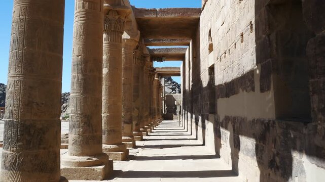 Perspective view of a corridor with ancient columns of an Egyptian temple named "Philae", close to the city of Aswan, Egypt. Sun on the left make linear columns shadows.