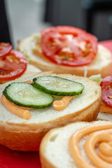assembling a burger from ingredients. sauce , cucumber and tomato on a bun