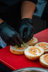 assembling a burger by a chef. bun with sauce and vegetables close-up