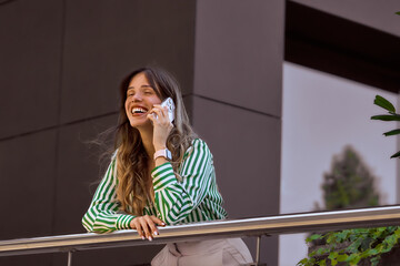 Smiling Woman Talking on the Phone Outdoors in a Modern Setting. Happy businesswoman talking on mobile phone on office balcony