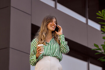 Professional Hispanic Woman Talking on Phone and Holding Coffee Outdoors in Modern Setting. Business person portrait on a bright daylight 