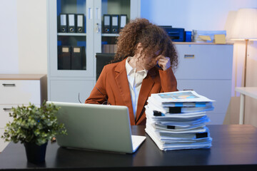 Tired young woman working late at the office, looking sleepy, using smartphone, wanting to relax,...