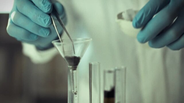 A scientist wearing gloves uses tweezers to place a filter in a funnel while conducting a filtration experiment