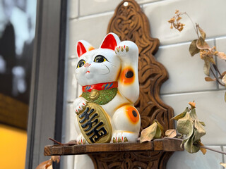 Maneki neko figurine with raised paw on wooden shelf. Tradition, prosperity, and cultural belief symbol in everyday lifestyle and decor.