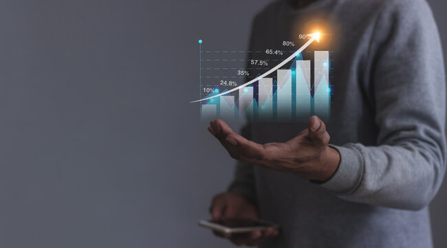 Young man with smartphone hand holding to visualize money growth The phone screen displays graphs and charts showing increasing investment and savings trends, along with an increased account balance