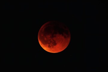 A striking close up of a blood moon glowing red against a stark black sky in the night time darkness