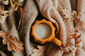 Mug of coffee latte, knitted woolen light beige sweater or plaid and dry oak leaves. Autumn, fall concept. Flat lay autumn composition.