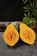 Fresh Cut Pumpkin Squash with Orange Flesh on Dark Kitchen Counter with Greens and Spices