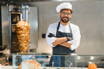 Chef smiling with arms crossed in front of shawarma rotisserie and display case