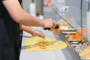 Chef adding grated carrots to shawarma with french fries in a street food stall