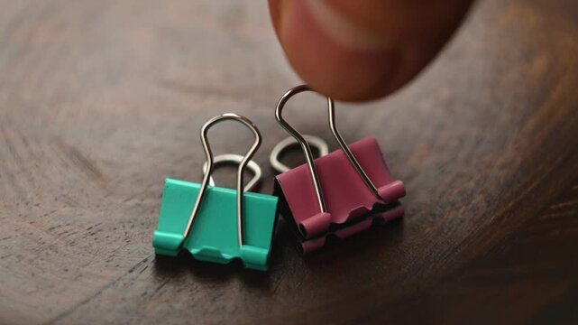 Fingers pick up a paper binder clip from wooden surface. Stationery concept. Macro shot.