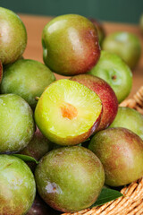 Fresh Green and Red Plums in Basket with Cut Half Showing Yellow Flesh