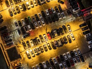Aerial view of a crowded outdoor parking lot with many cars illuminated by warm yellow lights at night © ABCDstock