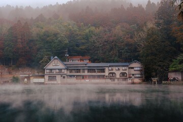 Fototapeta premium Serene lakeside Japanese inn with misty forest backdrop.