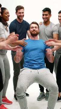 Diverse young adults in activewear perform a trust fall, supported by smiling teammates in a modern studio with bokeh. High-key light, slow dolly video. Concept of strong teamwork