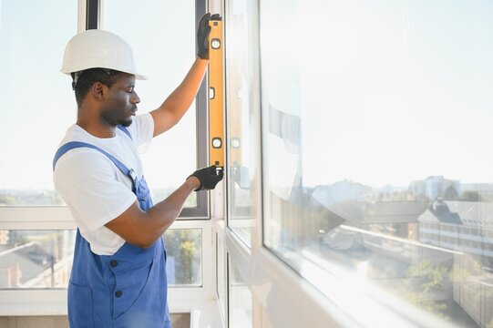 Young African Repairman In Overalls Installing Window