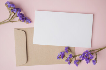 White blank greeting or invitation card with envelope and purple flower decoration on pink background.
