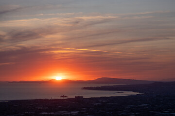 Sunset over the Gulf of Naples with dramatic clouds and city coastline view.