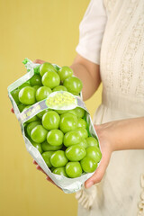 Woman Holding Fresh Green Grapes in Paper Bag on Yellow Background