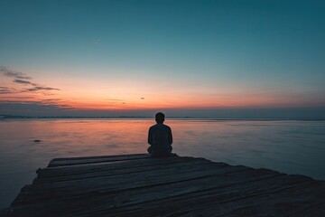 Silhouette of a person seated on a wooden dock, facing a tranquil sunrise over water