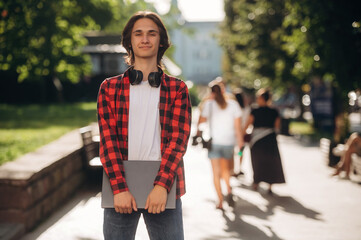 Standing and holding laptop. Young student is having a walk in the town