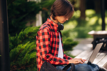 Side view, sitting with laptop. Male student is in the public park outdoors