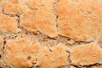 Close-up shot of the top crust of a freshly baked loaf of bread, showing its rustic, cracked surface and golden-brown color