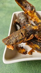 Fried catfish served in a white ceramic dish, isolated on a green wood texture background.