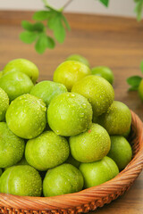 Fresh Green Plums in Wicker Basket on Wooden Table with Water Droplets