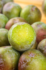Fresh Greenish Plums with Reddish Color - Ripe Stone Fruit Cut in Half Showing Juicy Yellow Flesh
